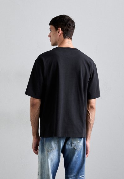 Black short-sleeve t-shirt with a relaxed fit, made from cotton. Worn with light blue distressed denim jeans featuring patchwork.