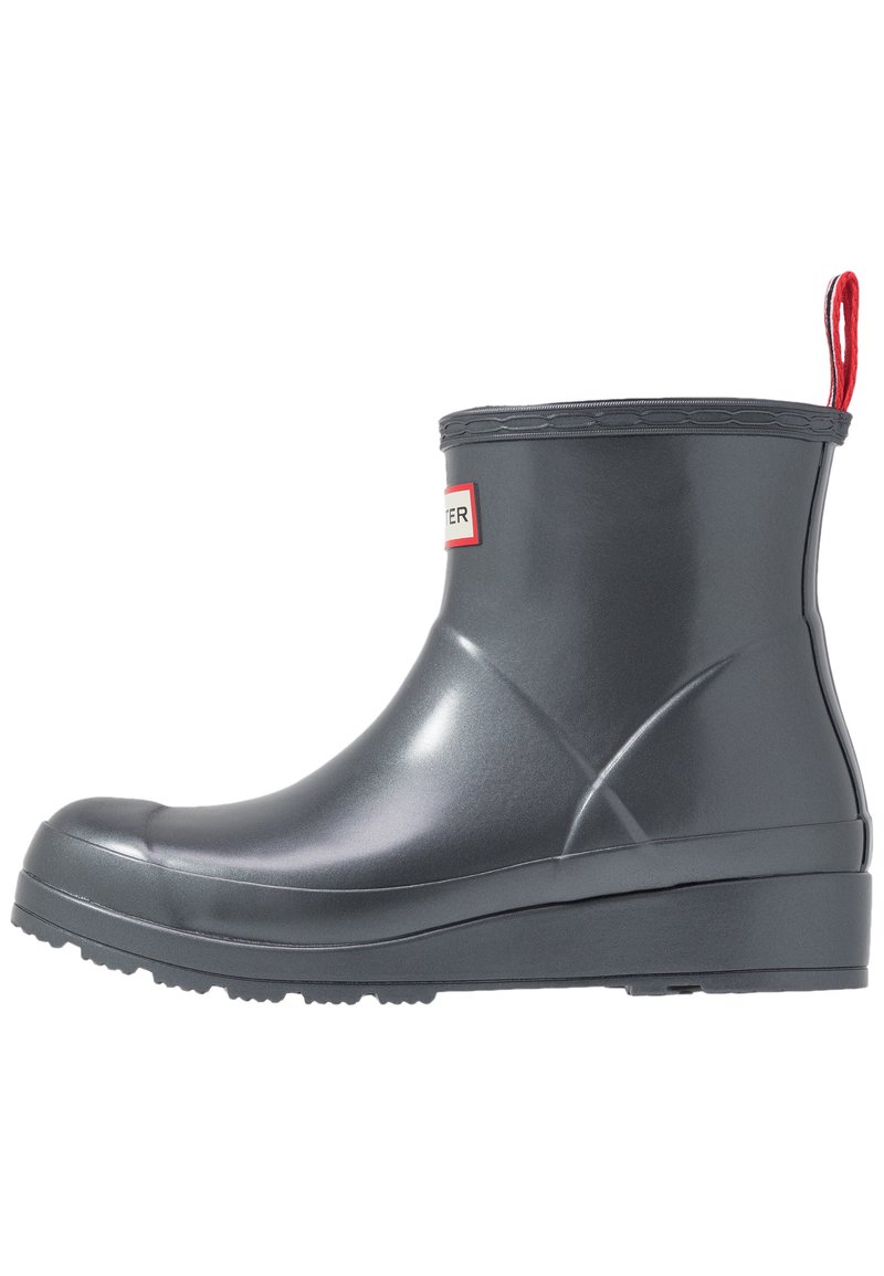 Bota de lluvia corta de goma gris oscuro con suela con dibujo, tirador rojo en la parte posterior y pequeño logo rectangular en la parte delantera.