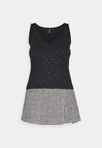 Svart linne med v-ringning prytt med silvernitar, kopplat till en kjol i svart och vitt houndstooth-mönster med plisserade detaljer.