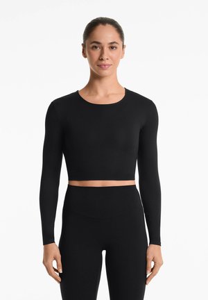 Un crop top noir à manches longues en tissu lisse avec un col rond, assorti à un legging noir taille haute de style ajusté.