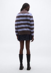 Barna és levendula színű vízszintes csíkos kötött pulóver magas nyakrésszel és bordázott mandzsettákkal, farmer szoknyával és térdig érő csizmával párosítva.