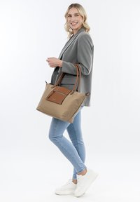 Borsa tote tan con dettagli in pelle marrone, manici superiori doppi e una tasca frontale con zip. Materiale in nylon liscio con una forma strutturata.