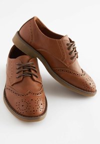 Chaussures en cuir marron avec une finition lisse, dotées de détails en forme d'aile, de perforations, d'un bout arrondi et de lacets marron contrastants. Semelle en caoutchouc.