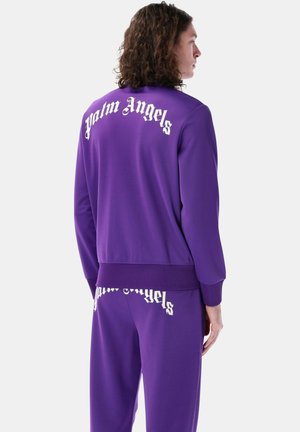 Tuta viola con lettering bianco "Palm Angels" sulla schiena e sulla gamba. Tessuto morbido, design slim, dettagli con polsini e vita a costine.