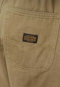 Beige katoenen stof met een achterzak voorzien van een zwart en gele label voor Jack & Jones, met gestikte randen en geweven textuur.