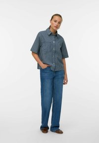 Camisa de botones de manga corta a rayas azul marino con cuello y bolsillo; combinada con jeans de pierna ancha azul y mocasines marrones.