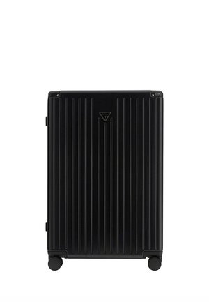 Valise rigide noire avec des rainures verticales, quatre roues et un logo Guess triangulaire centré à l'avant.