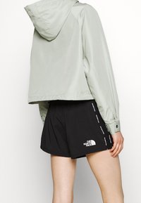 Jasnozielona wodoodporna kurtka z kapturem oraz czarne spodenki sportowe z białym logo i akcentami wzdłuż szwów bocznych.