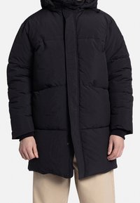 Schwarze Steppjacke mit Kapuze, einem gesteppter Design, Druckknopfverschluss und elastischen Bündchen, die eine warme und isolierte Passform bieten.