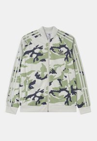 Chaqueta con cremallera de Adidas con un patr�ón de camuflaje verde y negro, tres rayas blancas en las mangas y el logo de Adidas en el pecho.