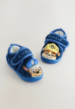 Blauwe pluche slippers met klittenbandsluitingen met ontwerpen van cartoonfiguren. De ene toont een politiemuts, de andere een bouwmuts. Zachte textuur.