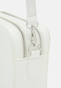 Borsa in pelle bianca texturizzata con hardware argentato, doppie cerniere e tracolla rimovibile. Presenta un dettaglio del logo impresso nella parte frontale.
