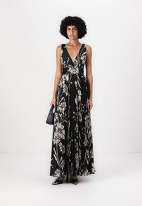 Robe maxi noire à fleurs avec décolleté V profond, texture plissée, motifs floraux rose clair et taille cintrée. Complétée avec des chaussures noires et un sac à main.