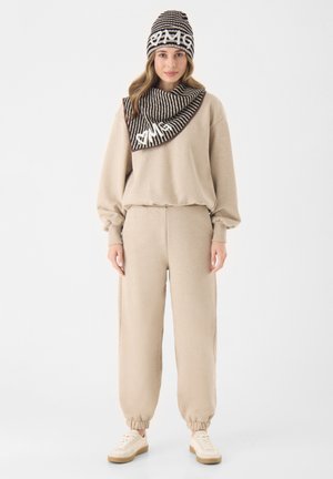 Beige sweatshirt en joggingsbroek met elastische boorden, gecombineerd met een gestreepte sjaal en muts met een wit logo. Casual gebreide textuur.