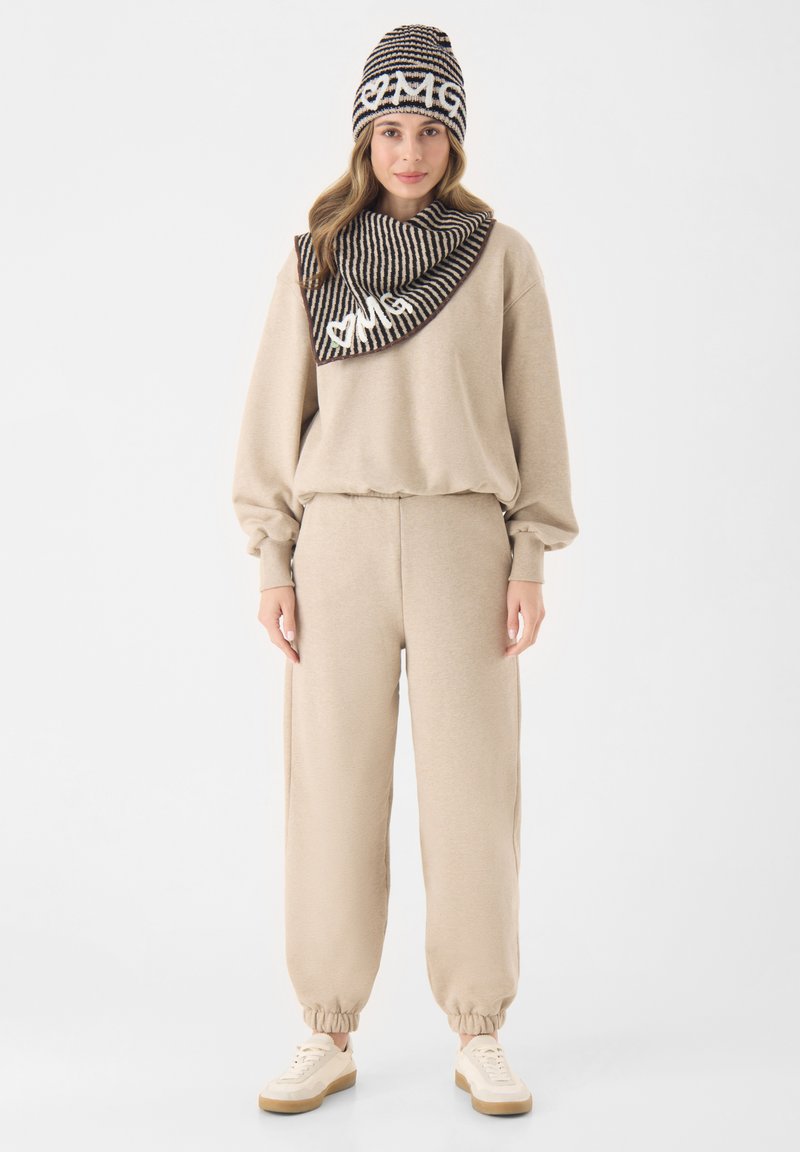 Beige sweatshirt en joggingsbroek met elastische boorden, gecombineerd met een gestreepte sjaal en muts met een wit logo. Casual gebreide textuur.