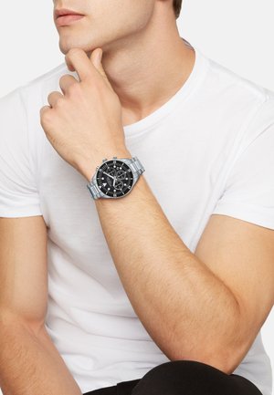 Montre en acier inoxydable argenté avec un cadran noir, dotée de grands marqueurs d'heure blancs, de sous-cadrans et d'un bracelet au style poli.