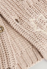 Beige gestrickte Strickjacke mit einem strukturierten Muster, einem gerippten Saum und einem runden Knopf aus hellem Material.