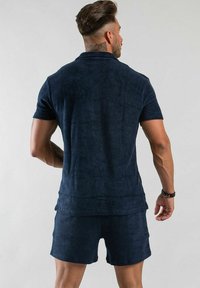 Mörkblå kortärmad pikétröja och matchande shorts, gjorda av mjukt tyg med en strukturerad yta. Avslappnad, lös passform.