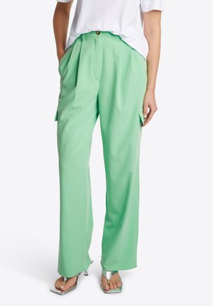 Groene geplooide wijde broek met zijzakken, gemaakt van een soepele stof, gecombineerd met open-toe metallic hoge hakken.