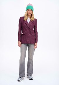 Podwójnie zapięta, ciemnofioletowa marynarka z wykładanym kołnierzem, dwiema przednimi kieszeniami, w połączeniu z szarymi dżinsami i wielokolorową dzianinową czapką.