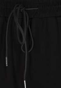Svart jogger midja med elastisk och justerbar dragsko; har silverfärgad spets på dragskon, slät textur och minimalistisk design.
