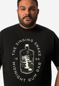 Černé bavlněné tričko s centrálním grafickým motivem láhve s palmou, měsícem a oceánem, doplněné bílým textem.