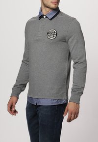 Graues Langarm-Polohemd mit rundem Kragen und Denim-Akzenten. Verfügt über ein rundes Logo auf der Brust und gerippte Bündchen.