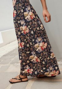 Maxi sukně z tmavě námořnické látky s květinovým vzorem, který zahrnuje růžové, červené a bílé květy. Plynulý design s úzkým pasem.