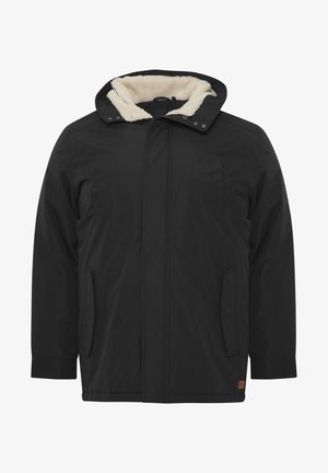 Veste noire isolée avec capuche. Elle est dotée d'une doublure en fausse fourrure, d'un zip à l'avant, de deux poches latérales et d'un petit logo sur l'ourlet.