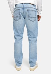 Jeans de mezclilla azul claro con corte recto, que cuentan con bolsillos traseros, costuras visibles y una textura ligeramente descolorida. Llevados con zapatos blancos.
