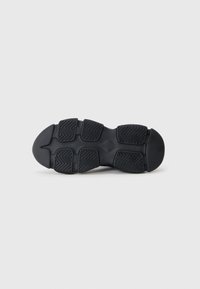 Semelle de chaussure en caoutchouc noir avec un motif texturé comprenant six sections distinctes, dont des rainures en zigzag pour l'adhérence. Design de bout arrondi et plat.
