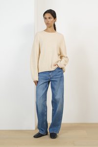 Beige, långärmad tröja i kombination med lösa blå jeans. Tröjan har en rundad halsringning och en mjuk textur, medan jeansen har en urtvättad finish.