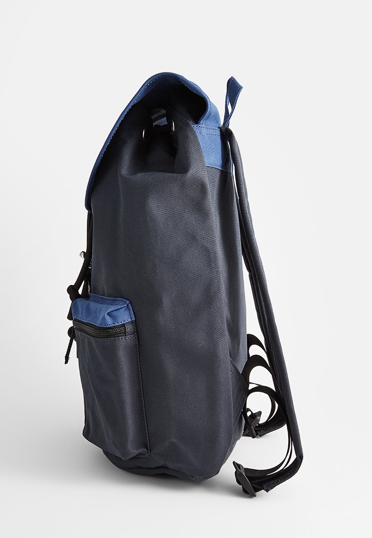 Rugzak in marineblauw met blauwe accenten, gemaakt van duurzaam materiaal. Beschikt over een voorzak met rits en verstelbare schouderbanden. Roltopontwerp.