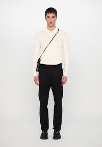 Krämfärgad stickad långärmad polotröja med platt krage, tillsammans med svarta byxor och en liten svart axelväska. Minimalistisk design.