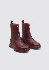 Botas de cuero burdeos hasta el tobillo con cremalleras laterales, acabado texturizado, punta redondeada y suela de goma gruesa y estriada. Cuenta con una tira en la parte posterior.