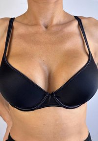 Sostén de tela negra con forma triangular, tirantes delgados ajustables y un detalle de moño en el centro. Textura suave y diseño minimalista.