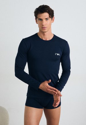 Camisa de manga larga azul marino y bragas a juego hechas de tela suave; presenta un pequeño logotipo blanco en el pecho, diseño ajustado y textura suave.