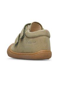 Beige semišová dětská bota se dvěma zelenými suchými zipy a texturovanou hnědou gumovou podrážkou, sledovaná z pravé zadní strany.