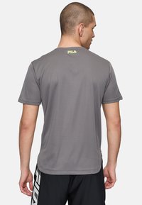 Camiseta gris de manga corta hecha de material transpirable. Cuenta con un escote redondo y un pequeño logo amarillo en la parte superior de la espalda.