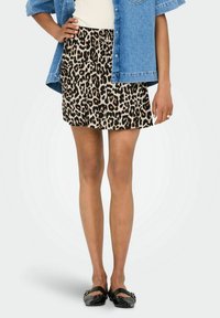 Mini-jurk met luipaardprint en een vloeiende vorm, met een neutrale beige achtergrond en zwarte en bruine vlekken. Gekleed met een denim overhemd met knopen.