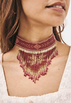 Collar choker de cuentas que presenta cuentas rojas y doradas, con un diseño de flecos y patrones intrincados en el cuello. Apariencia texturizada y en capas.