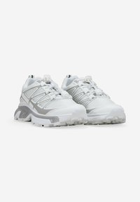 Par de zapatillas deportivas blancas con acentos grises, parte superior de malla y cordones de ajuste, posicionadas una al lado de la otra sobre un fondo blanco.