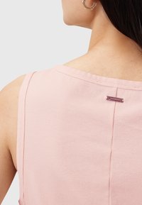 Vaaleanpunainen hihaton paita, jossa on teksturoitu kangas, näkyvä sauma ja pieni merkkilappu kaula-aukon lähellä selkäpuolella.