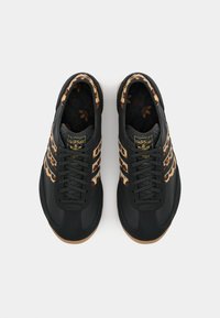 Black athletic shoes with a leopard print accent along the sides, featuring three striped branding, round laces, and a gum sole.