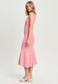 Rosa Strickkleid mit tailliertem Oberteil und ausgestelltem Saum, mit einem strukturierten Muster. Getragen mit hellen Blockabsatzsandalen.