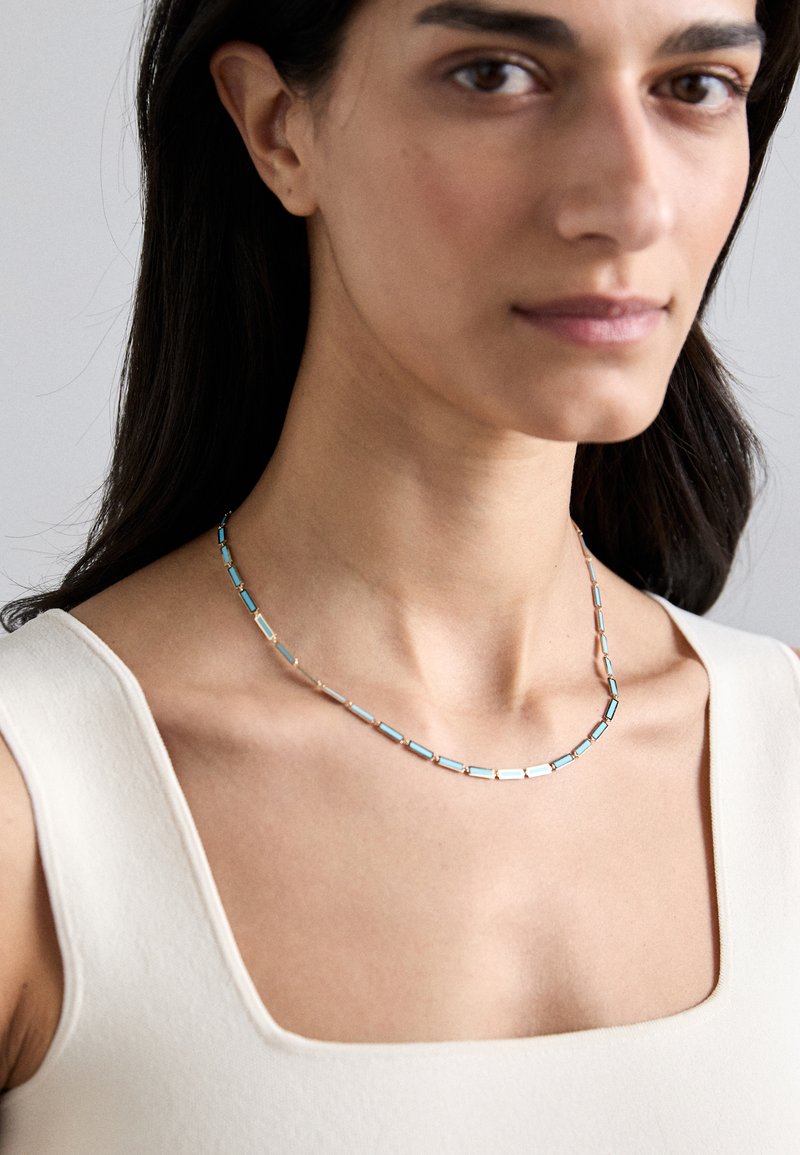 Sidabrinės spalvos karoliai, kuriose alternuojasi stačiakampiai jungiamieji elementai su turkio akcentais, glotnus paviršius ir paprastas, elegantiškas dizainas.