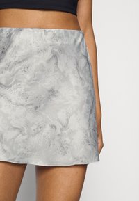 Mini-jupe en satin gris avec un motif texturé en spirale. Présente un ourlet droit et une finition lisse et brillante.