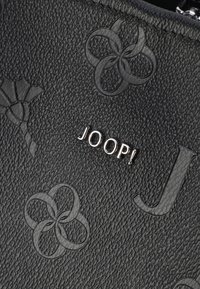 Svart texturerad läderväska med präglade blommönster och den metalliska "JOOP!"-logotypen i silver. Slät och förfinad yta.