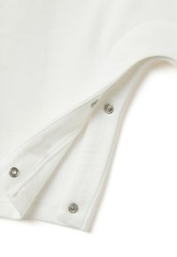 Weißes Baumwollkleidungsstück mit einem Druckknopfverschluss an der Seite. Der Stoff ist weich und glatt mit sichtbaren Nähten.