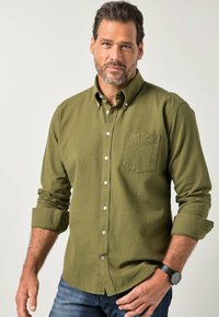 Olivgrünes Hemd zum Knöpfen mit strukturierter Oberfläche, ausgestattet mit einer Brusttasche und hochgekrempelten Ärmeln, kombiniert mit blauen Jeans und einer schwarzen Uhr.